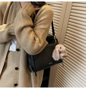Detail of minimalist black leather shoulder bag with cute plush rabbit charm on model