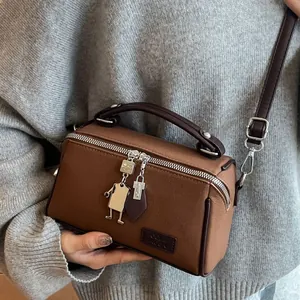 Borsa a tracolla marrone a scatola con manico e ciondolo a robot su sfondo di maglione grigio