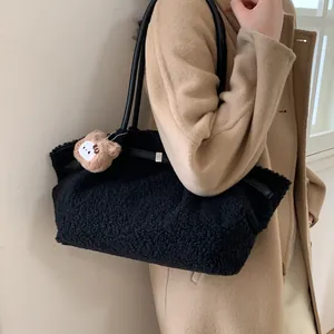 Large black fuzzy tote bag with leather straps and bear charm on woman in coat