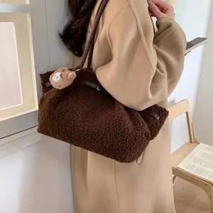 Large brown plush tote bag with shoulder strap and bear charm on beige cashmere coat