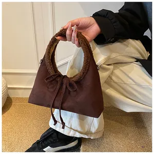 Dettaglio borsa in camoscio marrone con bordo in pelliccia sintetica e fiocco con nappe