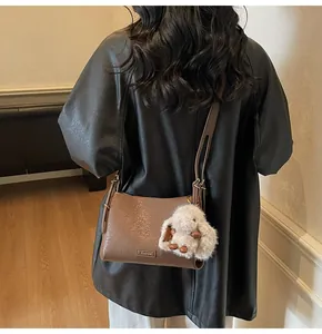 Detail of a brown leather shoulder bag featuring a cute beige plush bunny keychain accessory