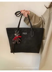 Close-up of black suede tote bag with contrast stitching and brown bear charm