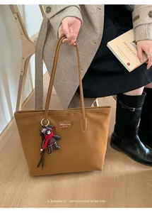Detail of a brown tote bag featuring a leather logo patch and a cute plush bear charm