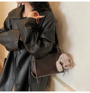 Detail of dark brown lychee texture leather bag with metal logo and plush rabbit charm
