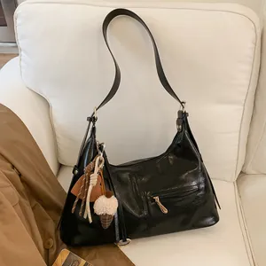 Sac hobo chic en cuir noir brillant avec détails dorés et breloques de sac stylées
