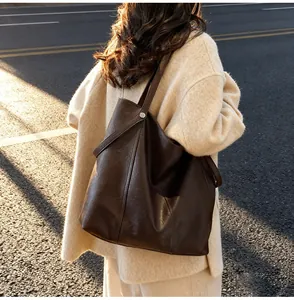 Close-up of a large dark brown leather tote bag with silver studs on a street background