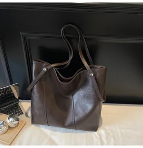 Macro detail of dark brown tote bag showing smooth leather texture and metal rivets