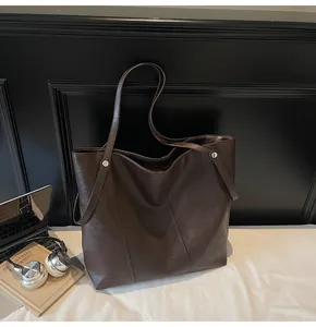 Detail of dark brown tote bag showing matte leather texture and silver rivet hardware