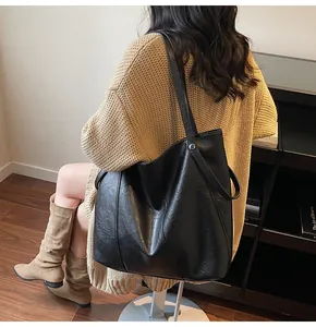 Detail of a large black textured PU leather tote bag shown on a shoulder in a cozy interior