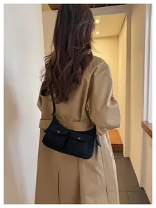 Detail of a chic black multi-pocket baguette bag with gold snaps on a khaki trench coat