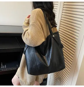 Side view of a large black leather tote bag worn by a model in a minimal indoor setting