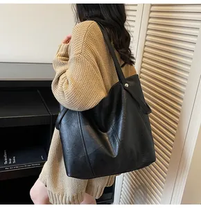 Detail of black leather tote bag showing slim shoulder straps and metal rivet hardware
