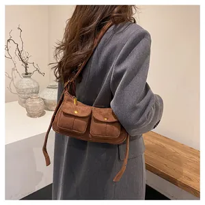 Close-up of brown suede baguette bag featuring dual front pockets and gold metal snaps