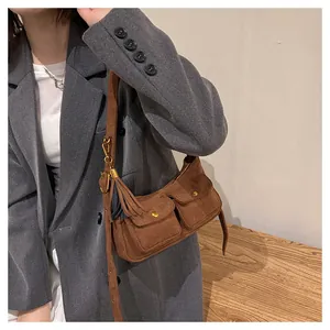 Close-up of brown suede baguette bag with dual gold buckle pockets and decorative tassels