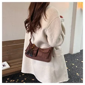 Close-up of brown suede baguette bag featuring front pockets and decorative long tassels