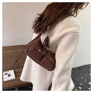 Detail of brown suede baguette bag featuring dual front pockets and long side tassels