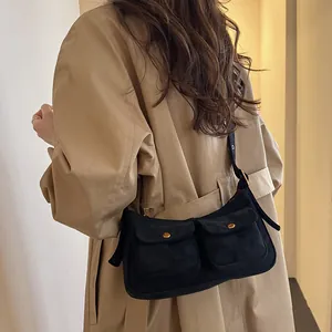 Minimalist black canvas shoulder bag with dual front pockets and gold buckle accents