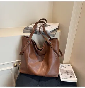 Detail of a brown leather tote bag with vertical stitching and silver rivet accents