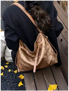 Close-up of bronze metallic tote bag with tan straps against autumn leaves background