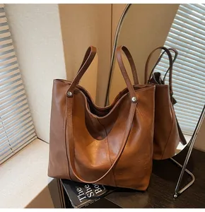Detailed view of brown tote bag showing leather texture, stitching and metal rivets