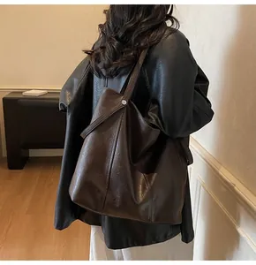 Close-up of a brown matte leather tote bag with wide shoulder strap and metal button