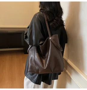 Side view of large dark brown leather tote bag worn by model in cozy interior setting