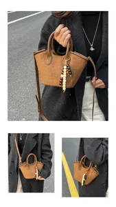 Detailed macro view of brown suede bucket bag with leather handles and beaded charm