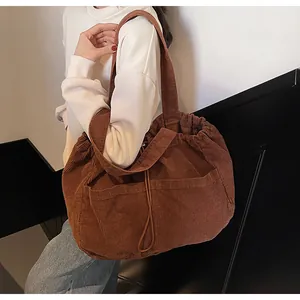 Sac à bandoulière en velours côtelé marron avec cordon de serrage porté par un mannequin