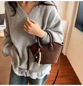 Close-up of brown suede handbag featuring miao she BAG embossing and wooden bead tassel