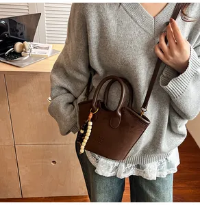 Detail of dark brown matte bucket bag featuring a wooden bead charm and handle