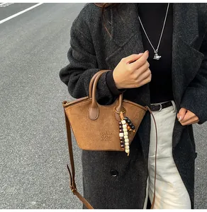 Detail of a brown suede bucket bag featuring a beaded tassel charm and logo embossing