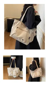 Detail of off-white canvas tote bag showing front zipper pocket and side storage pockets
