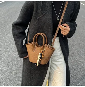 Close-up of brown suede bucket bag with colorful wooden bead charm and embossed logo detail