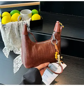 Close-up of brown woven hobo bag with wooden bead charm and silver zipper detail