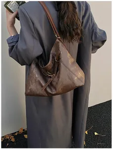 Detail of a brown glossy textured hobo tote bag featuring a metallic buckle strap and a sleek finish