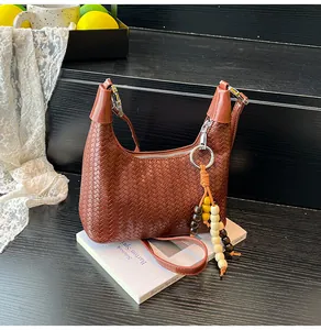 Detail of dark brown woven leather crescent bag with decorative wooden beaded tassel