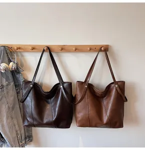 Detail view of large tote bags in dark coffee and tan leather on a wooden hanger