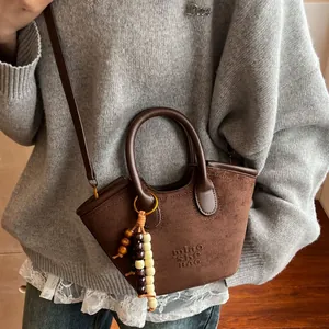Brown suede basket bag with beaded charm and leather handles for casual daily style