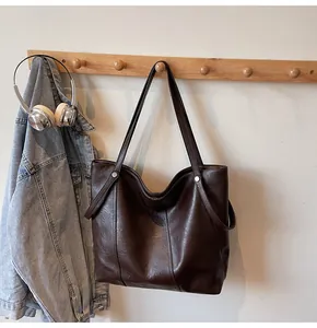Detailed view of dark brown leather tote bag with vintage texture hanging on a wooden hook