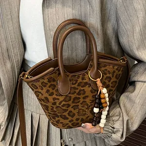 Chic leopard print bucket bag with leather trim and beaded tassel shown on a model