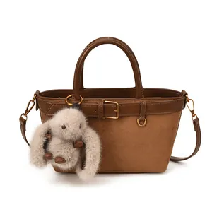 Détail d'un sac seau en daim marron avec bordure en cuir et porte-clés lapin gris