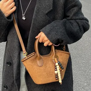 Brown suede basket bag with beaded charm worn by a model in a winter coat