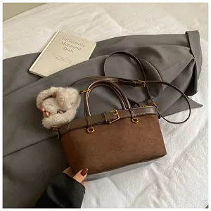 Détail du sac vintage marron avec texture mate, finitions dorées et pompon en peluche