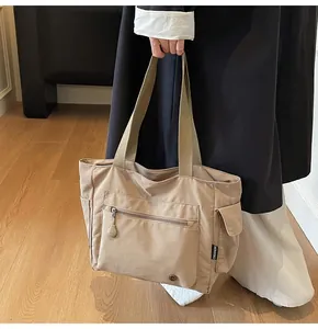 Close-up of khaki tote bag with zipper pockets, wide webbing straps, and durable fabric