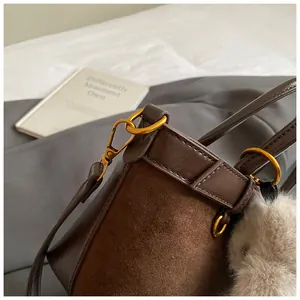 Détail du sac seau marron foncé mat montrant les coutures, les crochets dorés et le pompon
