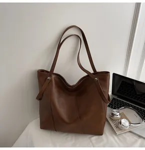Detail of a large brown leather tote bag showing matte texture and reinforced rivets