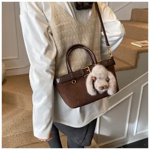 Détail d'un sac seau en daim marron avec un charm lapin en peluche beige et boucles dorées