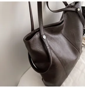 Detail view of large dark brown leather tote with silver rivets and minimalist texture