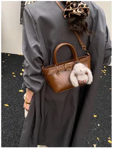 Détail du sac seau marron en cuir mat avec breloque lapin en peluche et poignées rondes